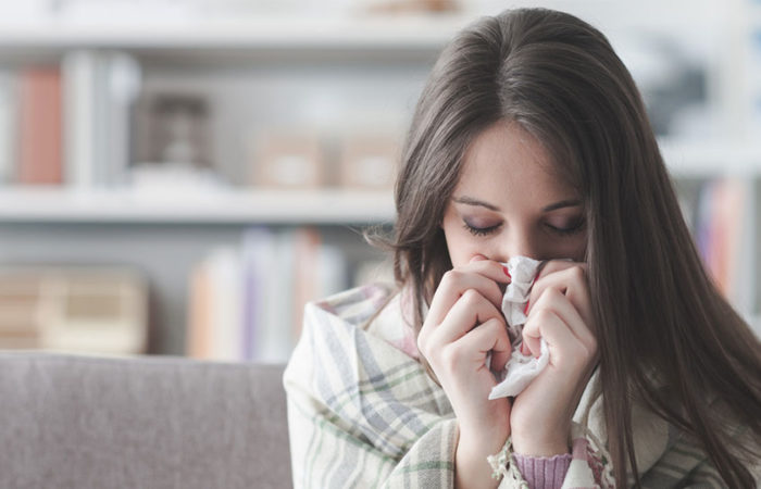 A woman with a blanket around her shoulders blowing her nose with a tissue.
