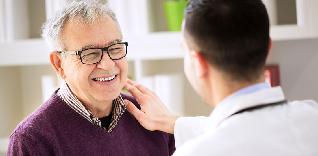 A doctor placing his hand on the shoulder of a smiling older man.