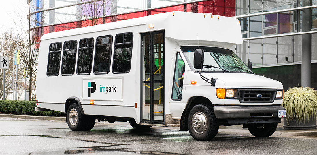 A clean and welcoming Impark HEALTH shuttle bus parked outside of a medical building.