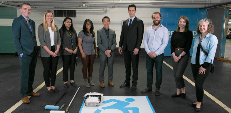 Representatives from Impark, The Forward Movement, and Holland Bloorview Kids Rehabilitation Hospital stand in a freshly painted parking stall featuring the Dynamic Symbol of Access (DSA).