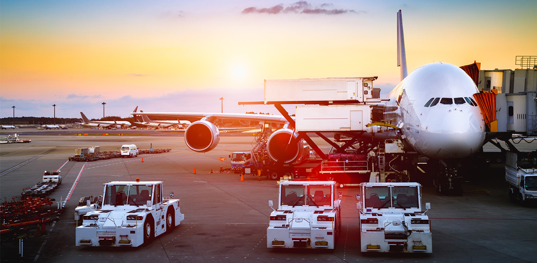 Stationary airplanes and luggage carts on an airport runway.