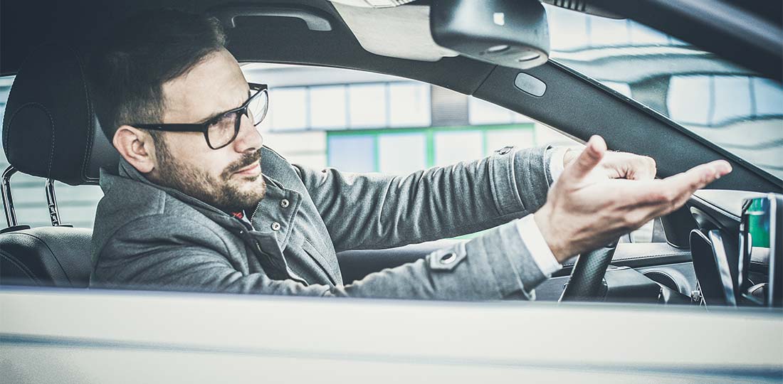 A visibly irritated man driving in a parking lot.